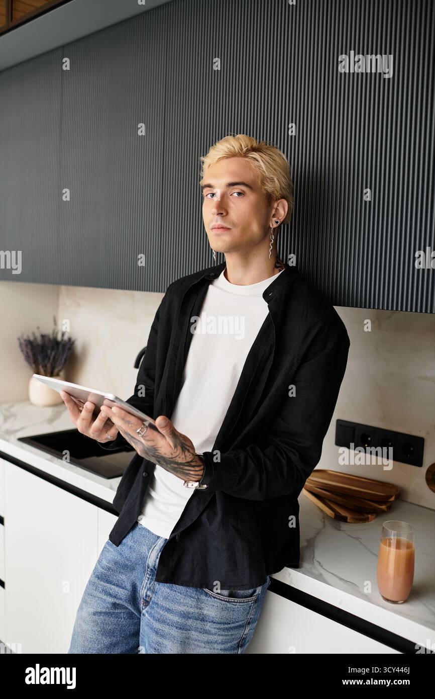 Un giovane affascinante si trova in una cucina moderna con un tablet, assaporando tranquille vibrazioni mattutine. Foto Stock