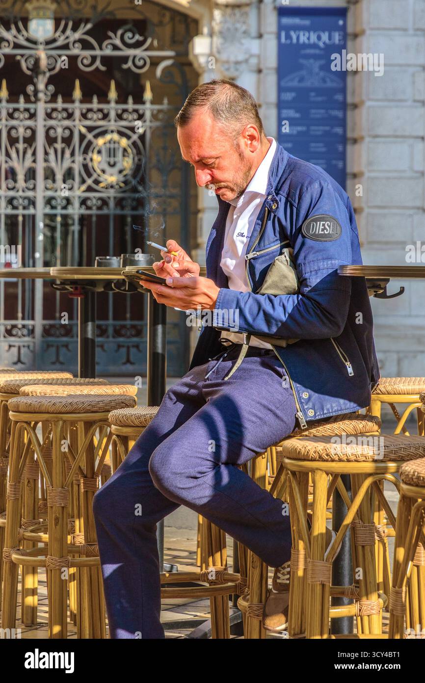 Il dipendente del ristorante durante la pausa mattutina era seduto sulla terrazza, fumava e guardava lo smartphone - Tours, Indre-et-Loire (37), Francia. Foto Stock
