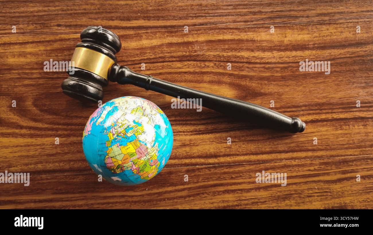 Il martelletto si trova in un piccolo globo mondiale su un tavolo di legno scuro, simboleggia il diritto internazionale, la giustizia globale, la politica ambientale e i diritti umani. Foto Stock