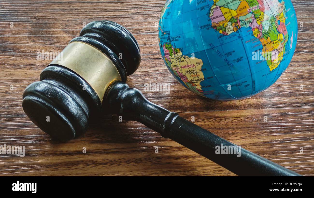 Il martelletto si trova in un piccolo globo mondiale su un tavolo di legno scuro, simboleggia il diritto internazionale, la giustizia globale, la politica ambientale e i diritti umani. Foto Stock