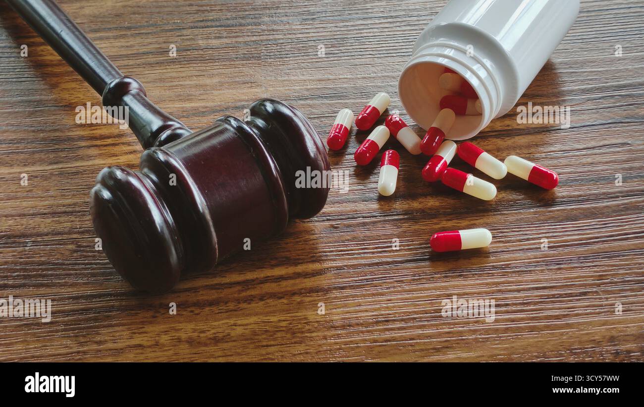 Martelletto e capsule farmaceutiche rosse e bianche versate su una superficie di legno scuro, che rappresenta negligenza medica, cause legali sanitarie e farmaci Liti Foto Stock