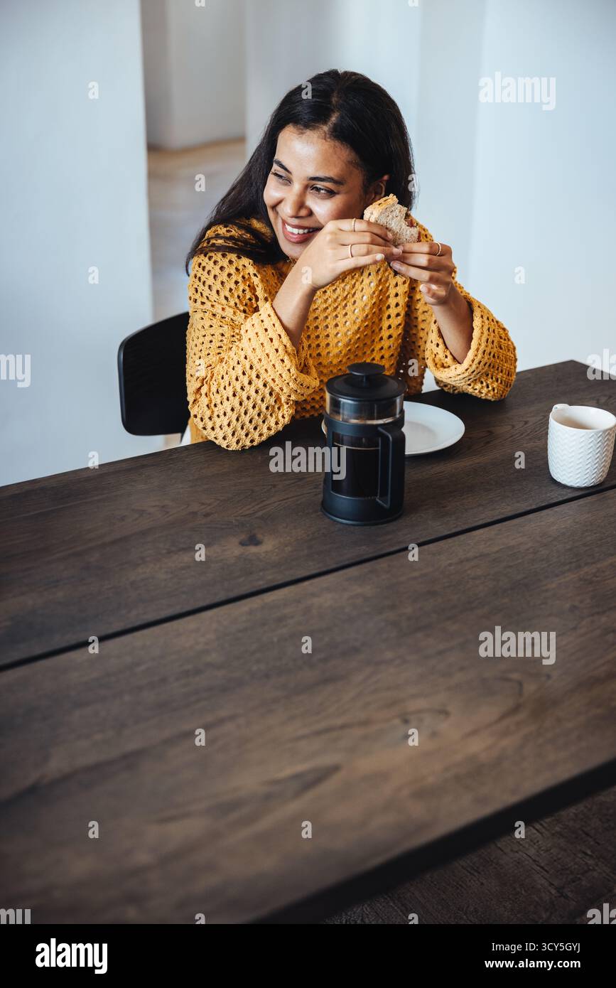 Una donna allegra si siede a un tavolo, assaporando un pasto con un caffè durante la pausa di lavoro. L'atmosfera è rilassante e mette in risalto un momento di pace in pennsylvania Foto Stock