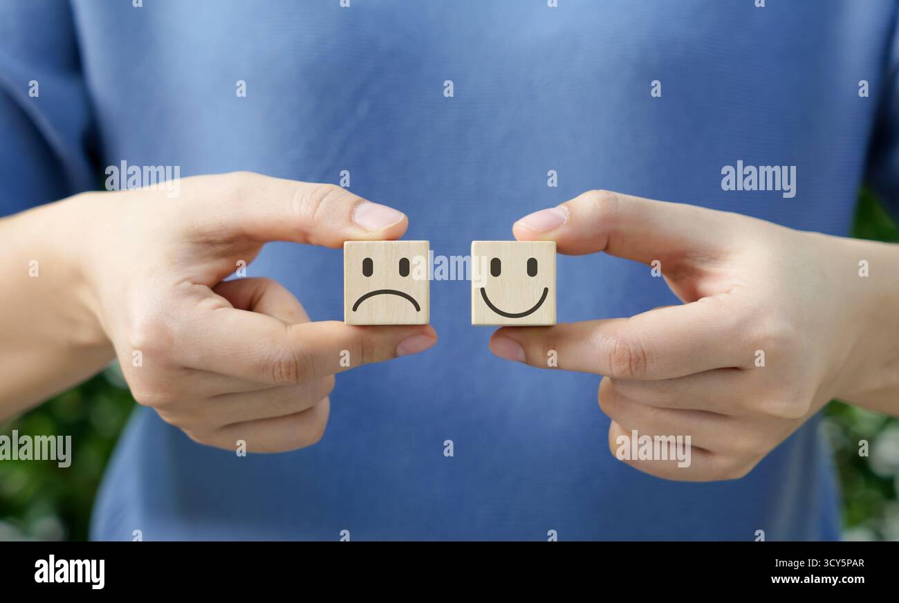 Scegliere le emozioni con il blocco di legno. Con cubi di legno con volti felici e tristi, il concetto di scegliere il tuo atteggiamento o emozione. Recensione del cliente Foto Stock