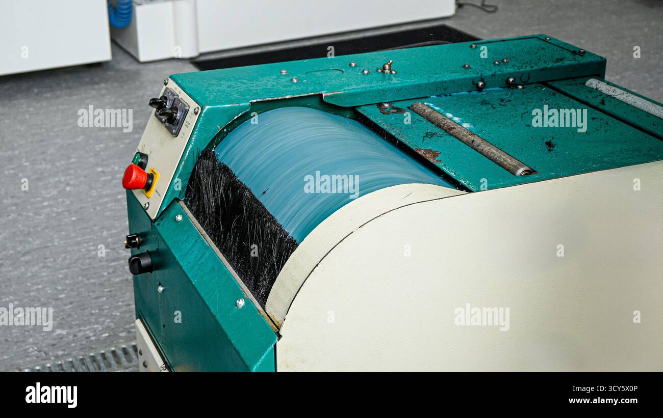 Macchina industriale che gira un rullo blu con una spazzola nera in fabbrica. Foto Stock