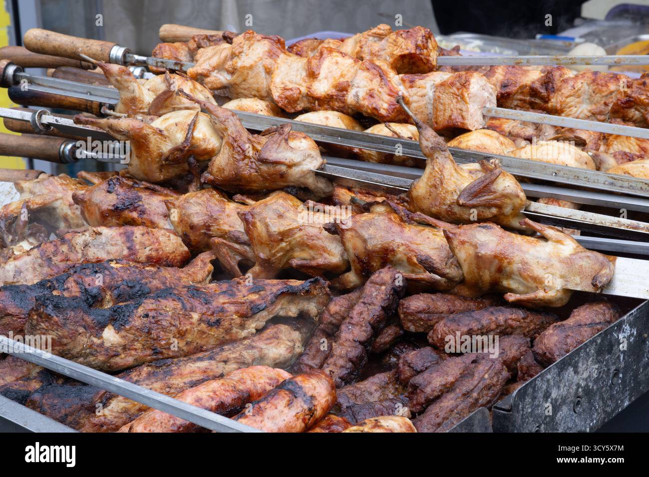 Carne alla griglia e quaglie arrostite sugli spiedini sopra i carboni caldi in un mercato di Street food, affumicato e marrone dorato. Foto Stock