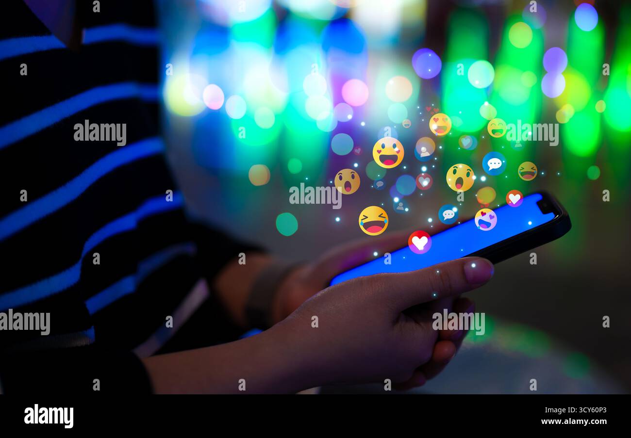 Concetto di tecnologia dei social media. Donna che utilizza uno smartphone con varie emoji colorate che fluttuano sopra lo schermo, simboleggiando l'interazione con i social media Foto Stock