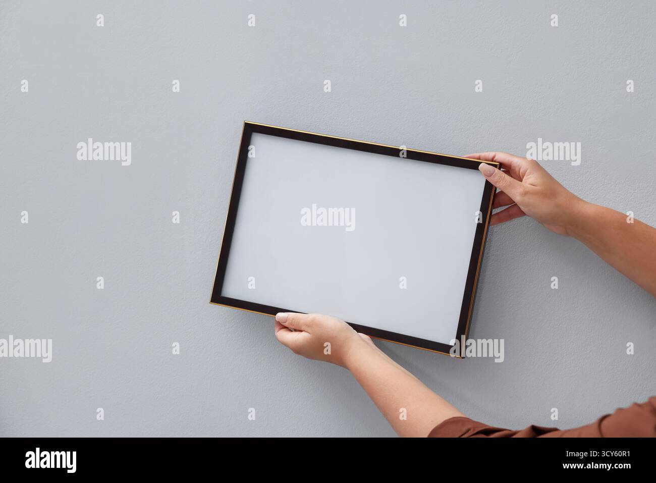 Donna che appende una cornice vuota per diplomi su una parete luminosa, primo piano. Mockup per il design Foto Stock