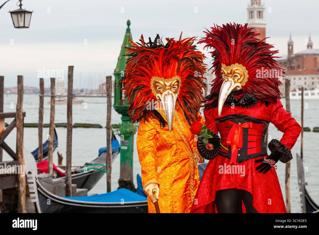 Carnevale di Venezia, Venezia, Veneto, coppia di favole che indossa costumi rossi e arancioni e maschere del dottore della peste piuma Foto Stock