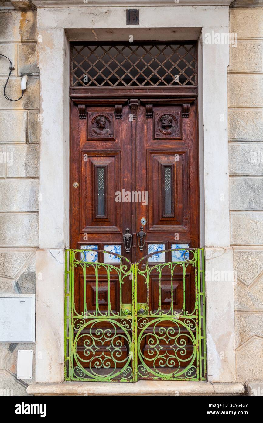 Una porta doppia ornata in legno scuro con busti intagliati e un poppa a motivi diamantati è incorniciata da pietra e fissata da un vibrante e verde battuto dagli agenti atmosferici Foto Stock