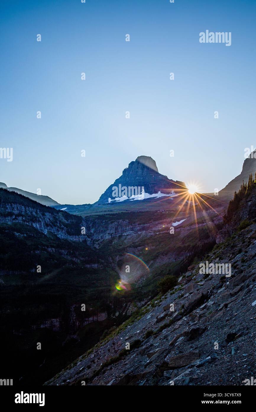 Il sole sorge alle spalle del monte Bearhat nel Glacier National Park, Montana, gettando una brillante stella attraverso la valle alpina. Questa vista sorprendente al Foto Stock