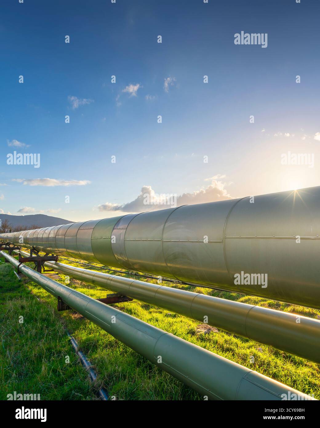 Grandi tubi di vapore isolati che trasportano energia geotermica presso lo stabilimento di Larderello in Toscana, Italia. Paesaggio industriale al tramonto che mette in mostra le energie rinnovabili Foto Stock