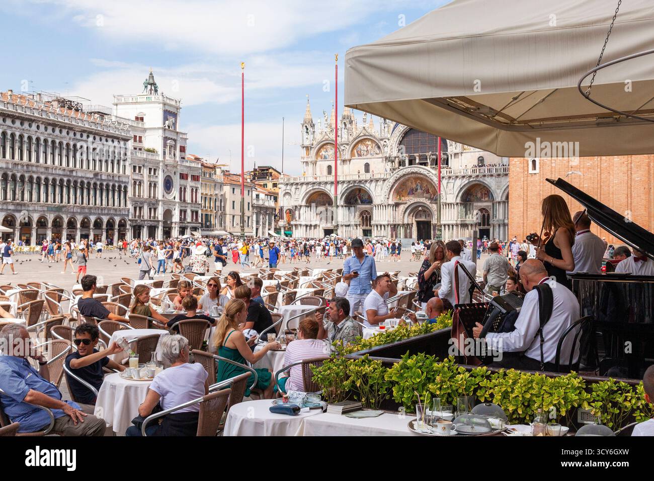 I turisti si godono bevande rinfrescanti e ascoltano musica dal vivo al caffè Florian, affacciato su Piazza San Marco e la Basilica, Venezia, Italia Foto Stock