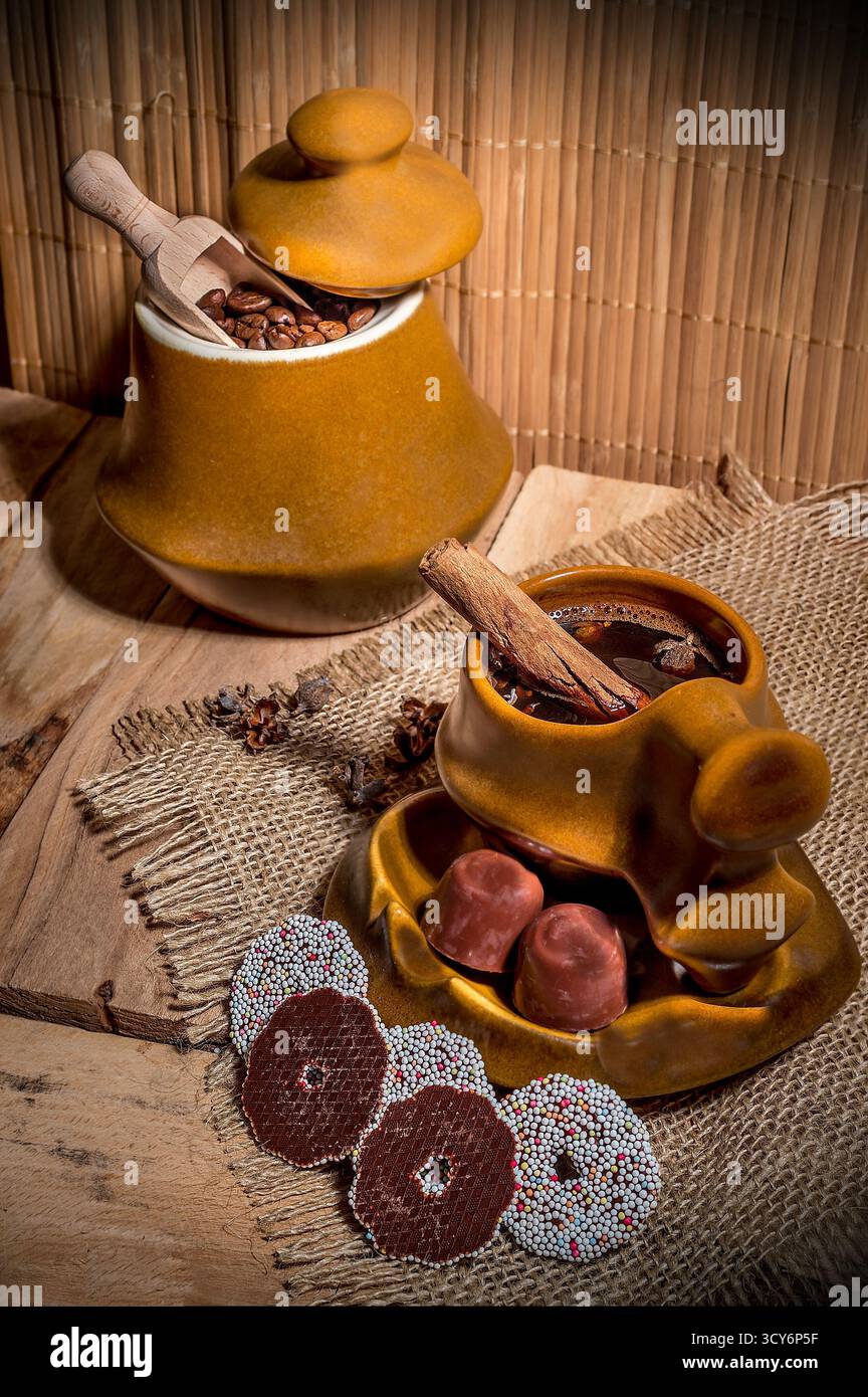 Ambiente rustico con chicchi di caffè, bevanda calda guarnita con cannella e anice stellato, tartufi di cioccolato e biscotti cosparsi. Foto Stock