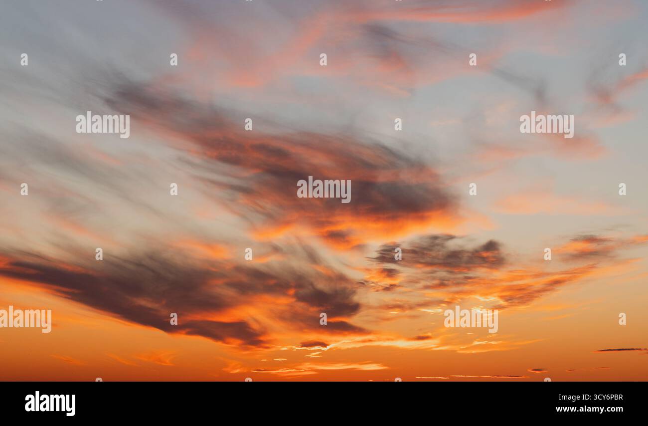 Una scena mozzafiato al tramonto presenta calde nuvole arancioni che si spostano attraverso un cielo tranquillo, dipingendo l'orizzonte con luce dorata. Perfetto per la natura, tr Foto Stock