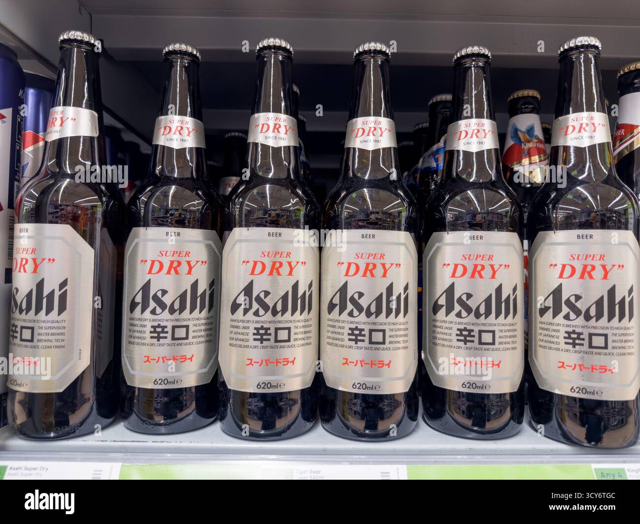 Una fila di sei bottiglie di birra Asahi è ordinatamente disposta su uno scaffale nel corridoio dell'alcol di un supermercato di Londra, pronto per l'acquisto. Foto Stock