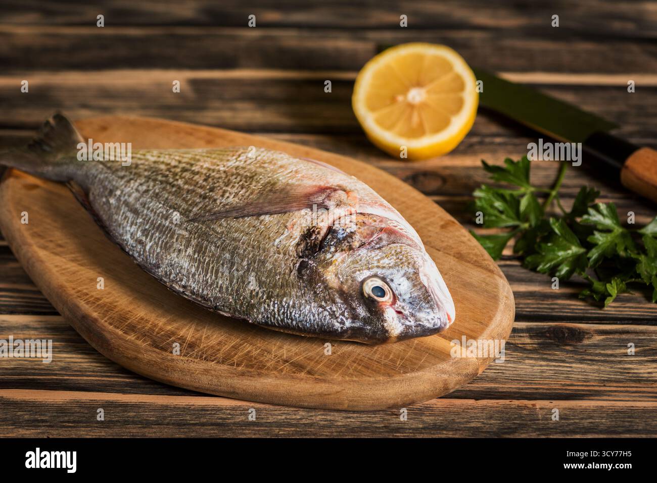Orata fresca con testa dorata preparata per la cottura su un tagliere di legno Foto Stock