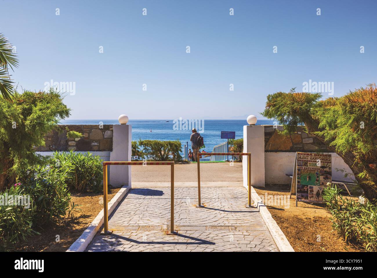 I turisti che scendono dall'uscita dell'hotel alla spiaggia del Mar Egeo sullo sfondo di un cielo azzurro. Kos. Grecia. Foto Stock