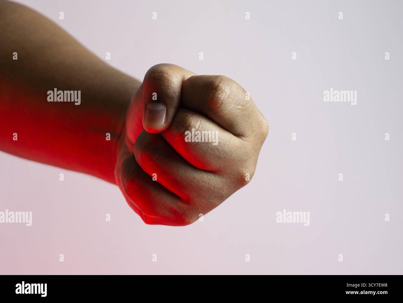 Mano maschile agganciata al pugno su sfondo bianco con illuminazione ambientale rossa, forte concetto di gesto catturato in una configurazione minimale e spettacolare da studio Foto Stock