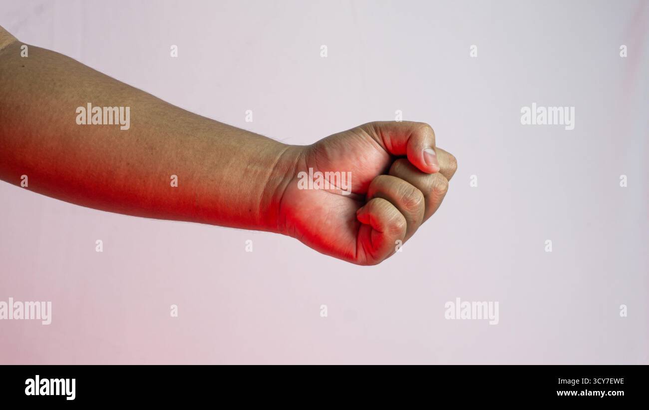 Mano maschile agganciata al pugno su sfondo bianco con illuminazione ambientale rossa, forte concetto di gesto catturato in una configurazione minimale e spettacolare da studio Foto Stock