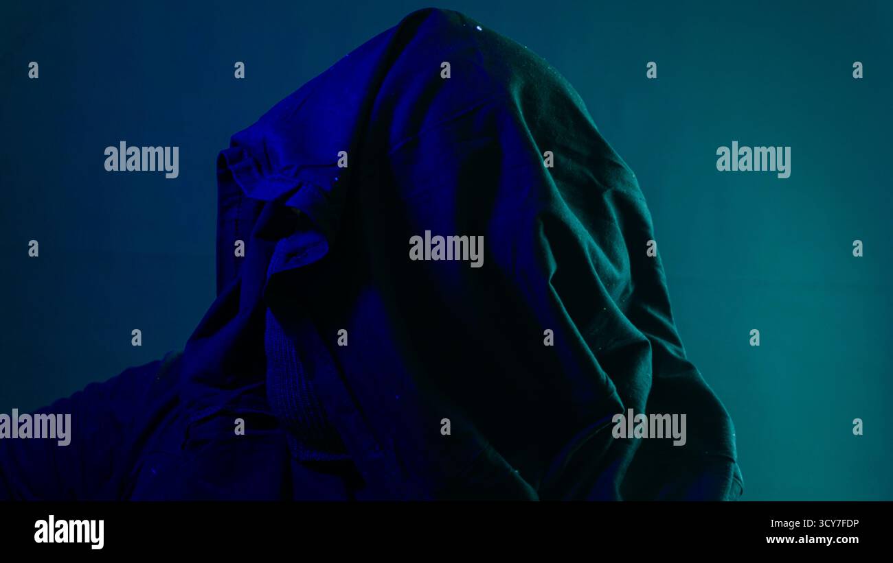 Misteriosa figura laterale illuminata da luce ambientale blu e verde su sfondo nero, silhouette ombrosa che evoca intrighi e concetto di identità nascosta Foto Stock