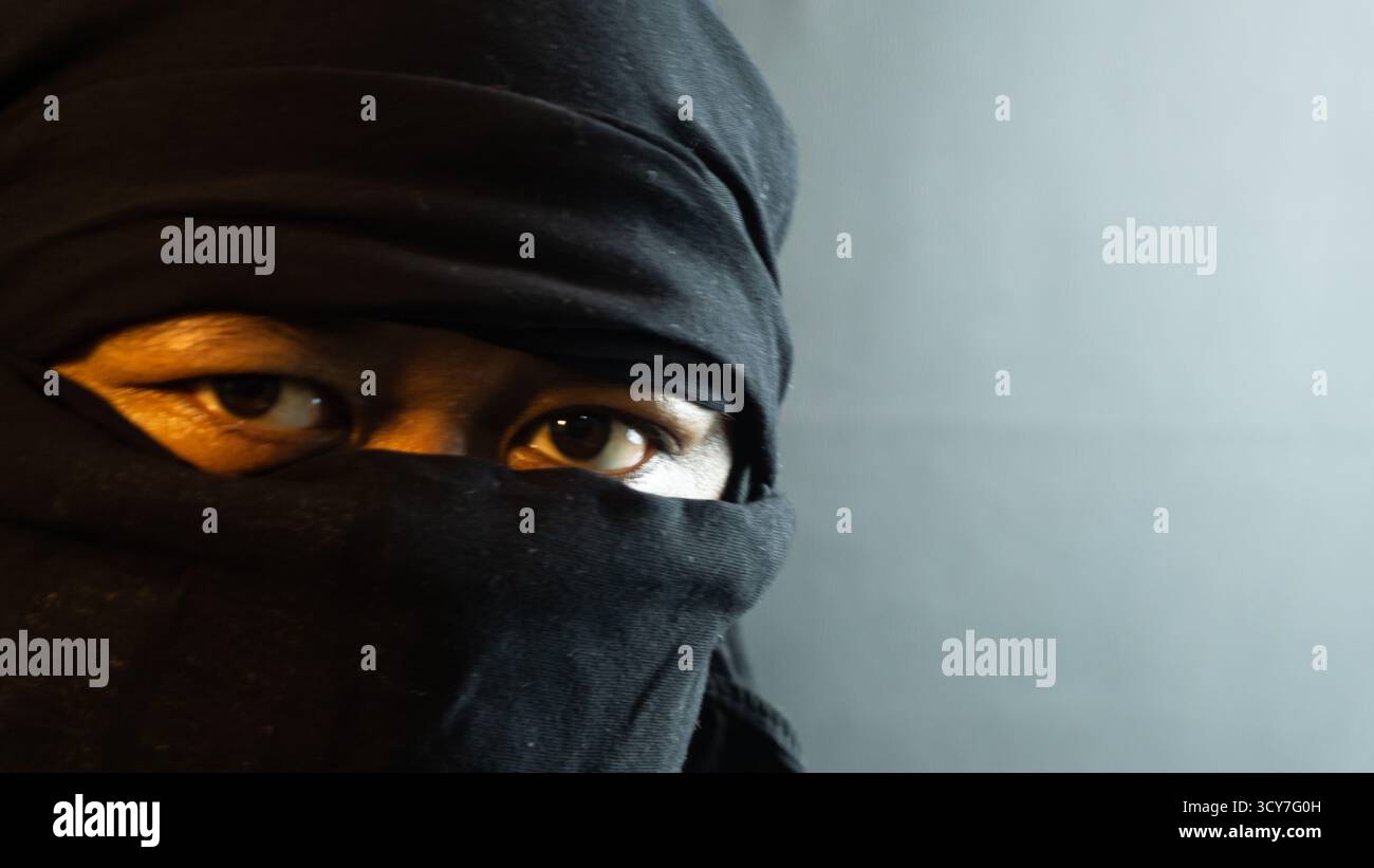 Primo piano di un viso maschile mascherato illuminato da una calda luce ambientale su sfondo nero, un look suggestivo e riservato che ricorda uno stato d'animo furtivo o ispirato ai ninja Foto Stock