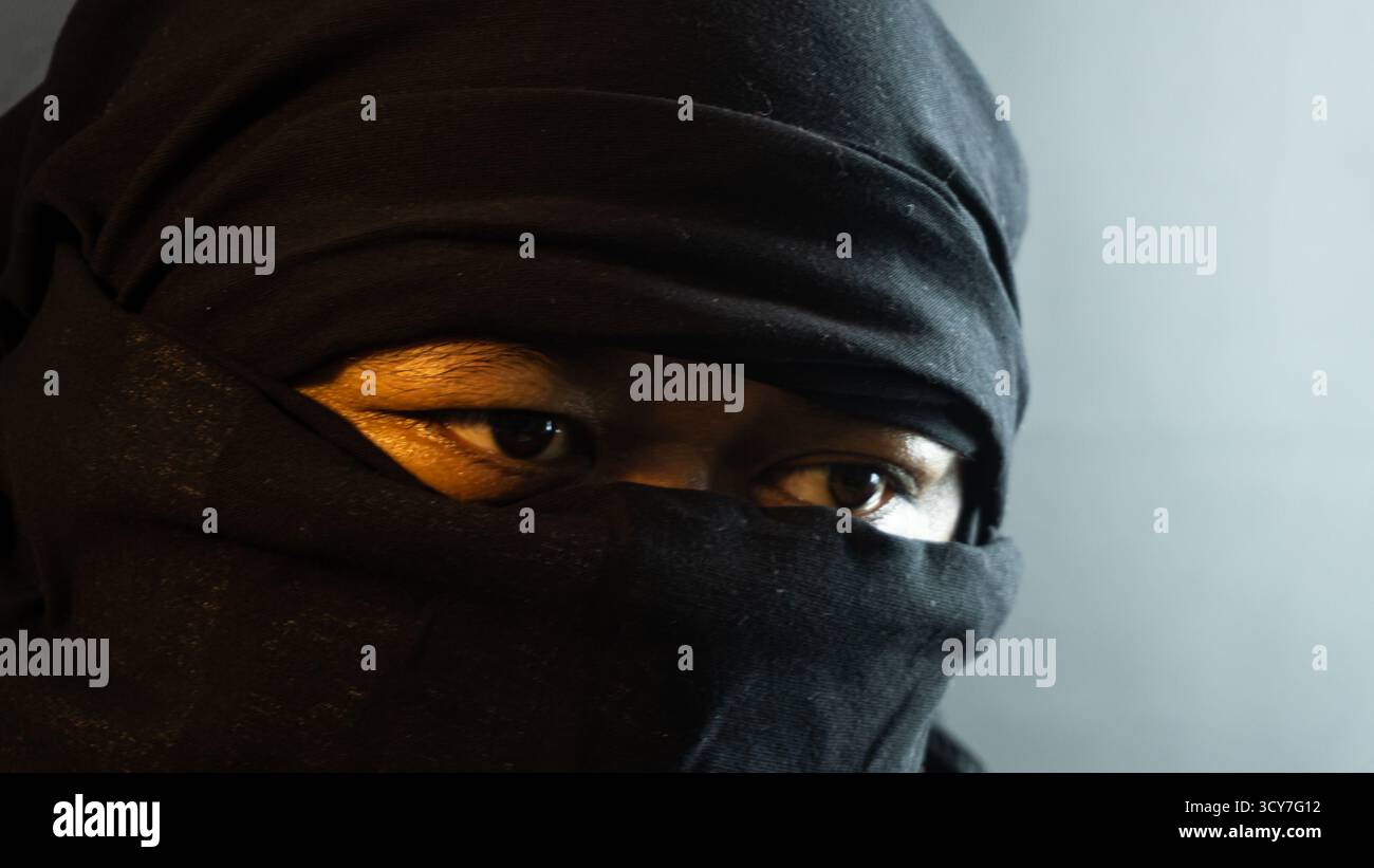 Primo piano di un viso maschile mascherato illuminato da una calda luce ambientale su sfondo nero, un look suggestivo e riservato che ricorda uno stato d'animo furtivo o ispirato ai ninja Foto Stock