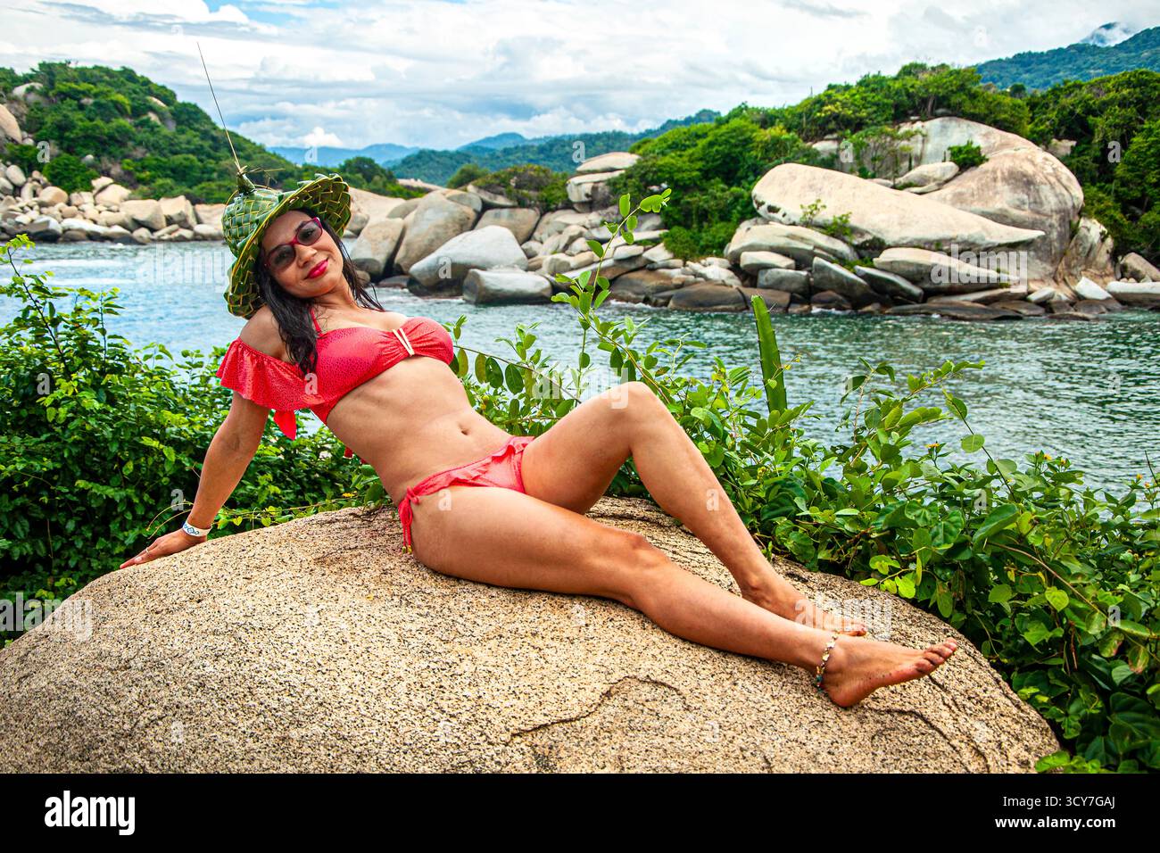 Giovane donna che indossa un cappello e un costume da bagno rosso, in posa nel Parco Nazionale di Tayrona, Colombia. Modello latino colombiano. Donna dai capelli scuri sulla spiaggia. Bruna. Foto Stock