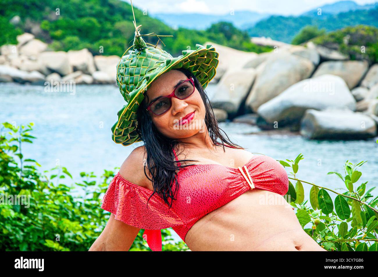 Giovane donna che indossa un cappello e un costume da bagno rosso, in posa nel Parco Nazionale di Tayrona, Colombia. Modello latino colombiano. Donna dai capelli scuri sulla spiaggia. Bruna. Foto Stock