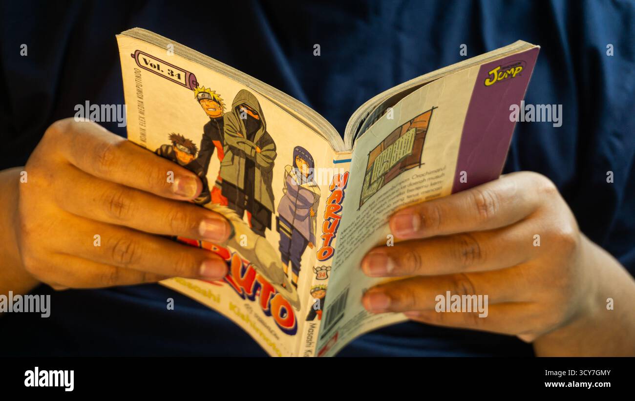 South Kalimantan, Indonesia - 07 21 2025 : Naruto manga aperto e tenuto per mano dell'uomo sotto una calda illuminazione, vista dettagliata delle pagine dei fumetti all'interno durante Foto Stock