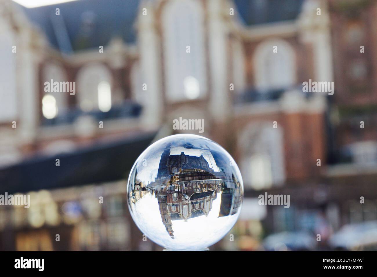 Sfera di cristallo davanti ad una facciata storica che mostra una strada del canale invertita e la torre della chiesa, catturata con profondità di campo bassa e luce pomeridiana. Foto Stock