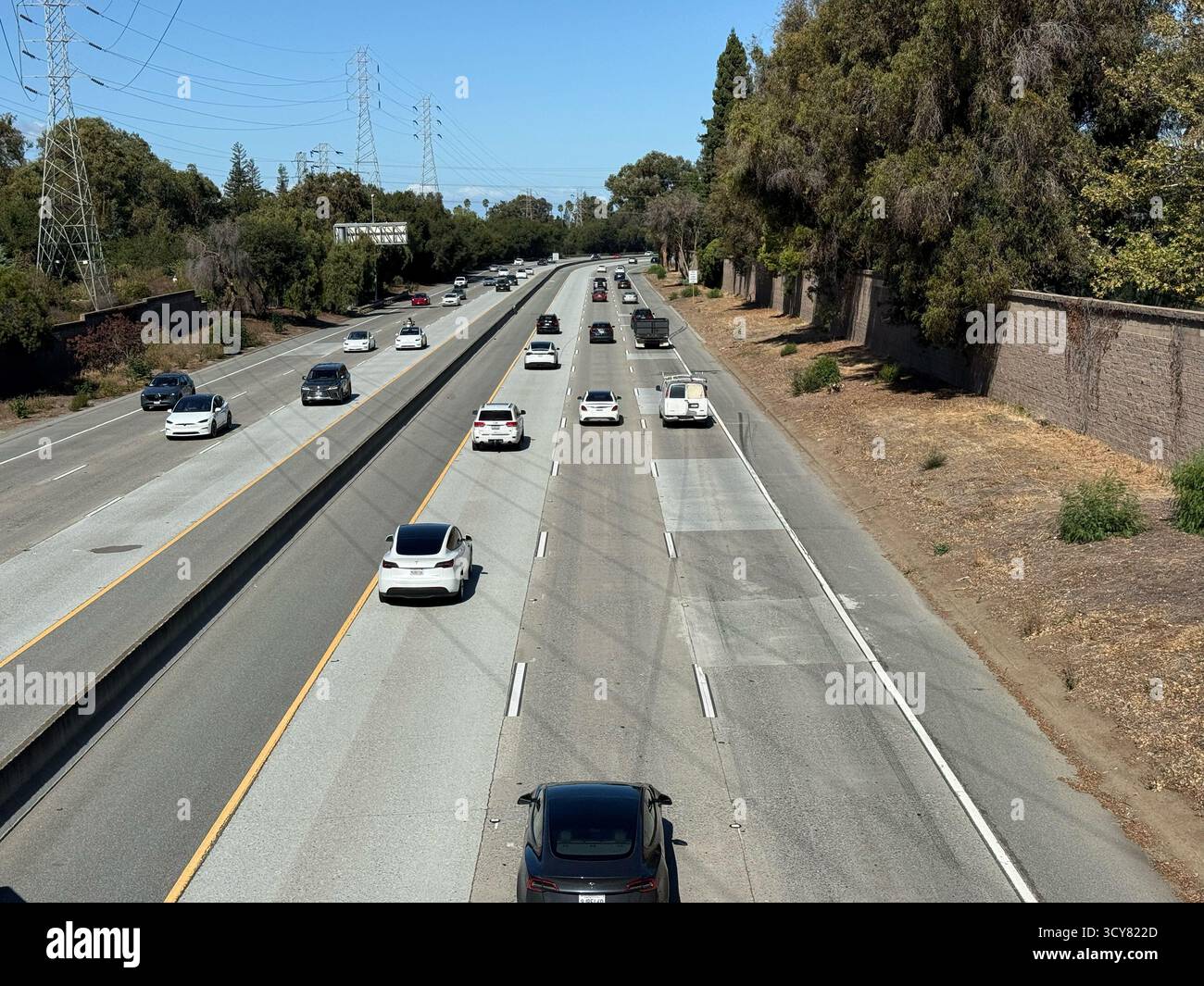 Vista dal cavalcavia pedonale che mostra le auto che guidano lungo l'autostrada 85 a più corsie circondata da alberi, pareti insonorizzate e torri di trasmissione - montagna vi Foto Stock