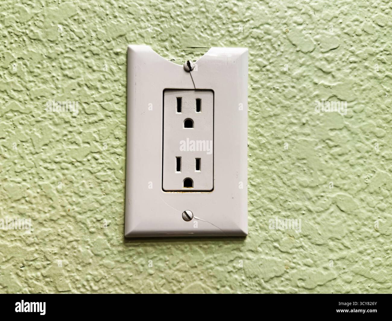 Presa elettrica rotta con piastra di copertura scheggiata e sfondo a parete in stucco verde testurizzato, che indica la necessità di sostituzione e illustra l'insp. Di sicurezza Foto Stock