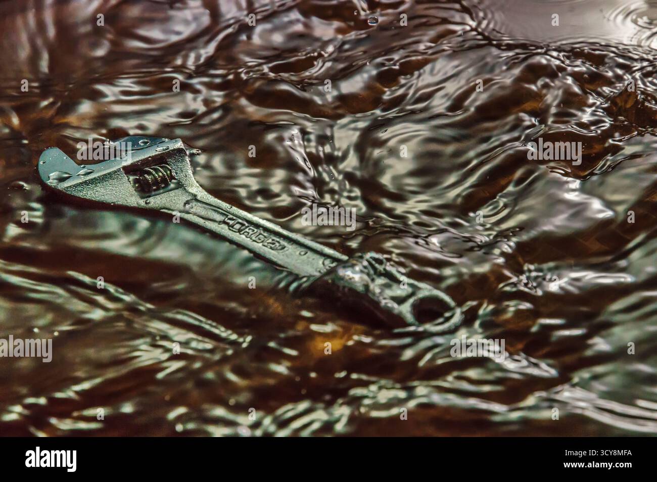 La chiave metallica contrassegnata con "FORCE" si trova in posizione piatta in acqua torbida. Increspature e riflessi creano una superficie con trama. Foto Stock
