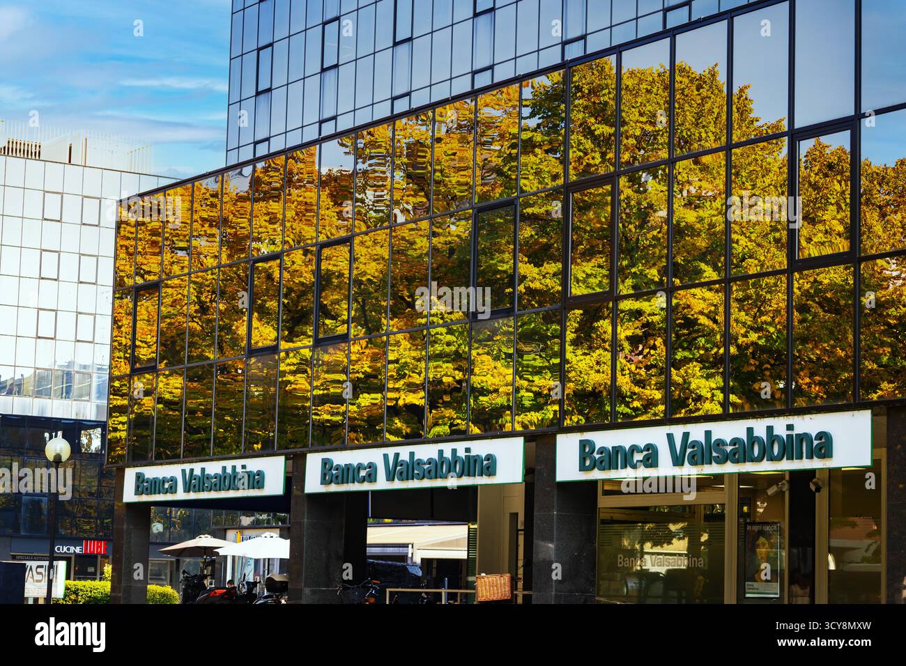 Un moderno edificio in vetro riflette alberi d'autunno dorati creando un suggestivo contrasto visivo tra natura e architettura contemporanea. Foto Stock
