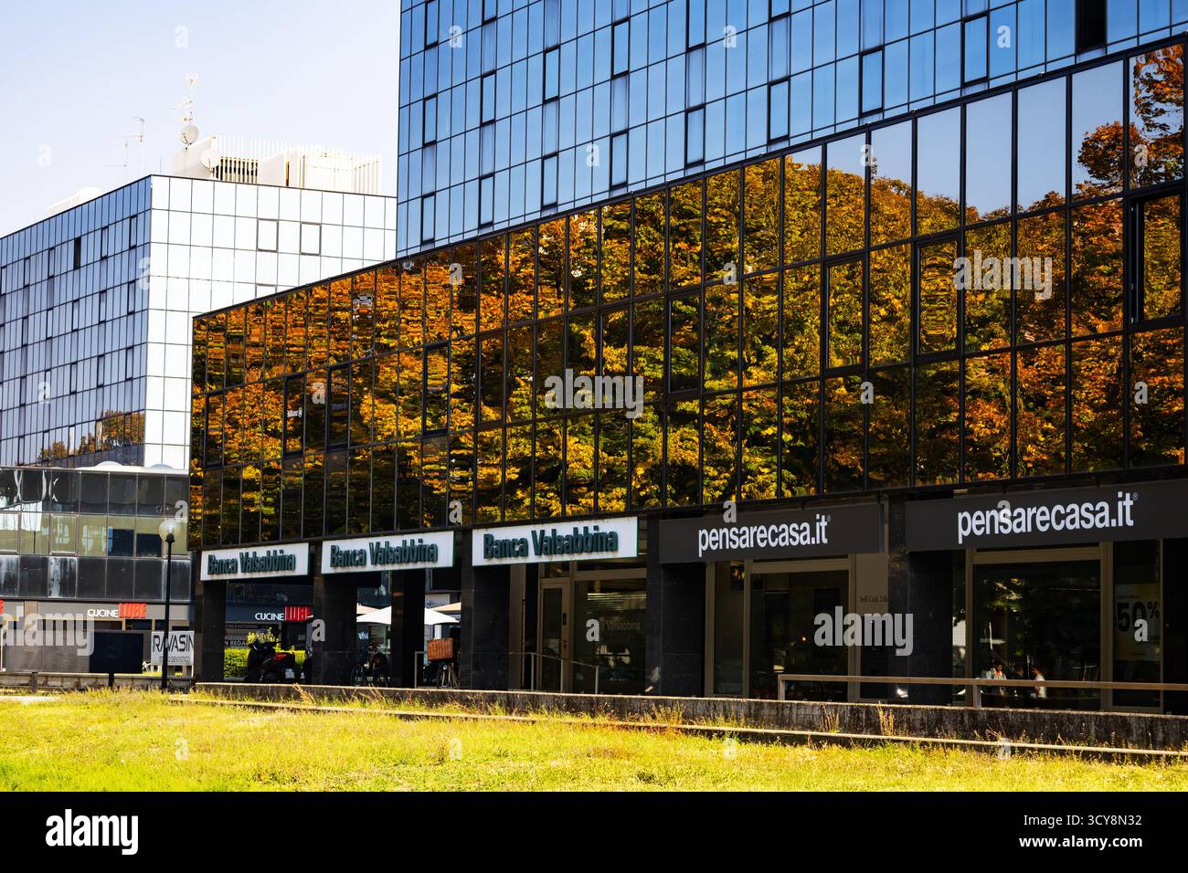 Un moderno edificio in vetro riflette alberi d'autunno dorati creando un suggestivo contrasto visivo tra natura e architettura contemporanea. Foto Stock