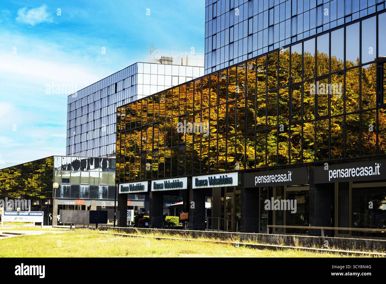 Un moderno edificio in vetro riflette alberi d'autunno dorati creando un suggestivo contrasto visivo tra natura e architettura contemporanea. Foto Stock