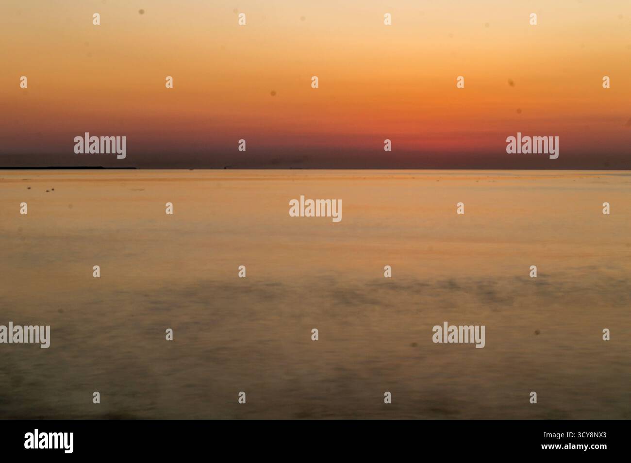 Mare calmo al tramonto in Romania. Il cielo caldo e sfumato si riflette sull'acqua liscia, creando una scena costiera serena e minimalista. Foto Stock