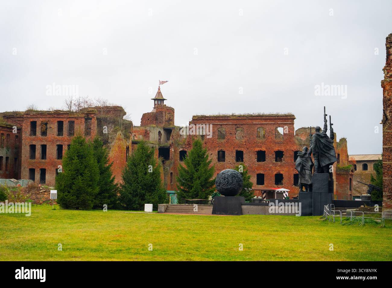 Ammira il cortile erboso verso una statua e le ampie pareti in mattoni rossi decomposizione degli edifici della prigione della Fortezza di Oreshek Foto Stock