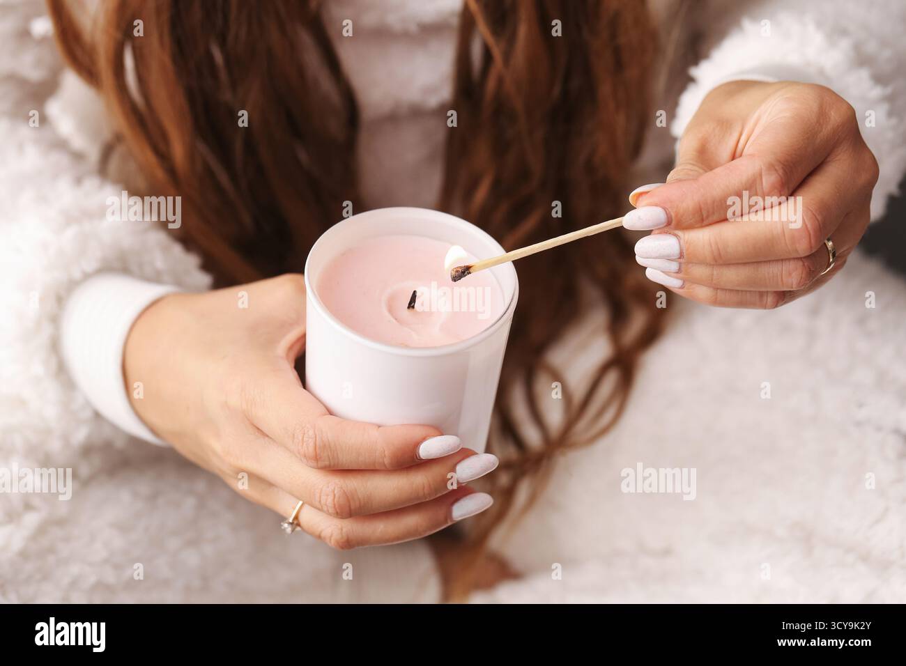Donna che accende candele profumate con fiammifero. Accogliente atmosfera casalinga con candele aromatiche e caldo umore invernale. Concetto di relax e cura personale. Foto Stock
