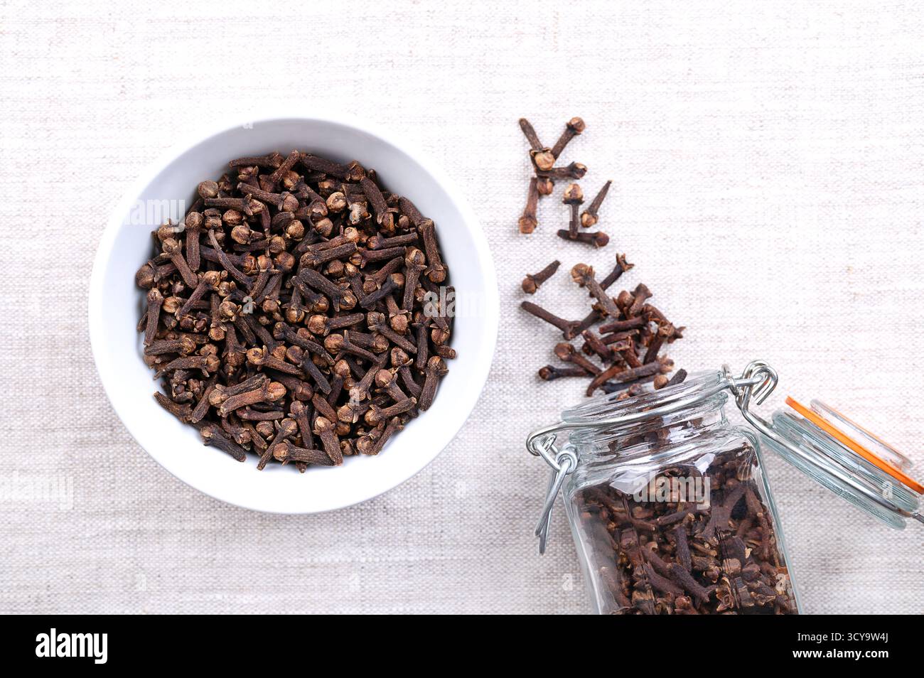 Chiodi di garofano secchi, in un recipiente bianco, su lino. Boccioli di fiori aromatici dell’albero Syzygium aromaticum, utilizzati come spezia, fragranza e per aromatizzare. Foto Stock