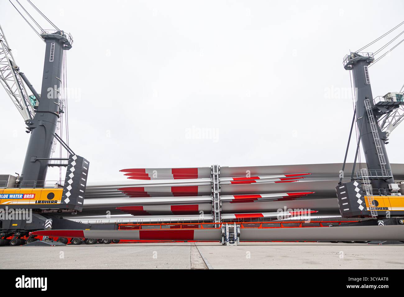 Cuxhaven, Germania - 01.28.2023: Scarico di pale di generatori eolici da una nave da carico mediante due autogru portuali Liebherr. Foto Stock
