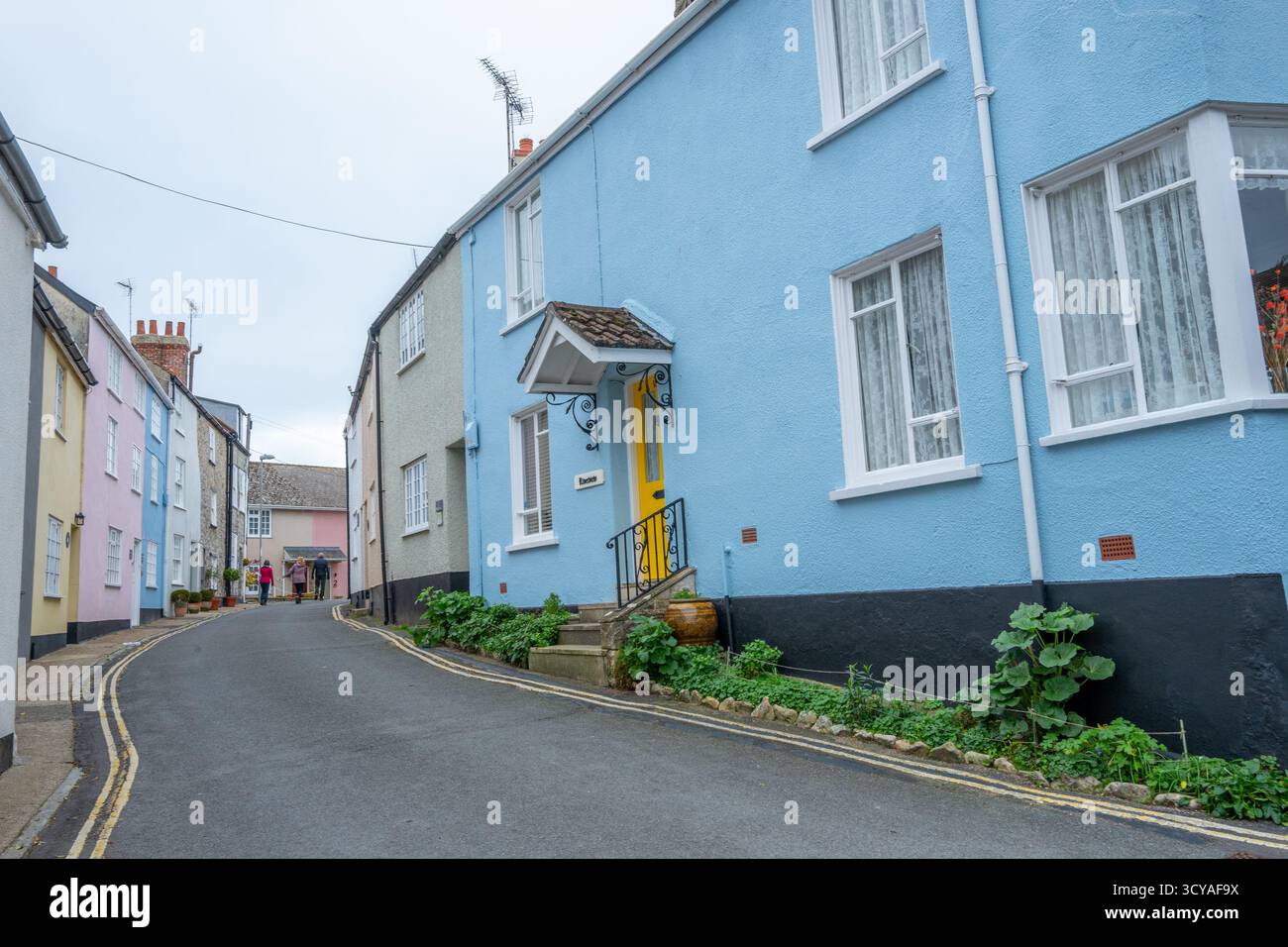 Case dipinte a pastello lungo la stretta corsia e dipinte di giallo sul parcheggio a doppia linea Mill Green nella città balneare di Lyme Regis, Dorset. Foto Stock