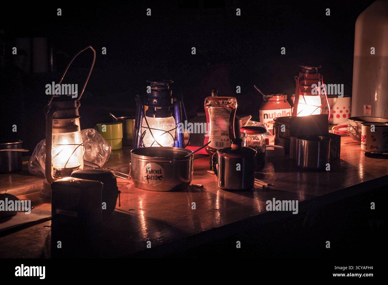 Tavolo da campeggio illuminato da lampade a cherosene con tazze, pentole e cibo durante una notte di campeggio invernale a Ješkova VES, Slovacchia. Foto Stock