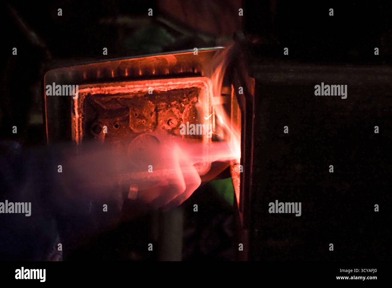 Persona che dà da mangiare legna da ardere in una stufa metallica illuminata durante una fredda notte invernale in un campo di osservazione a Ješkova VES, Slovacchia. Foto Stock