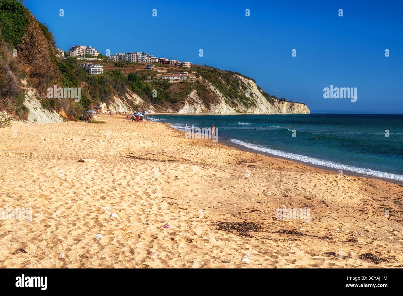 Byala, Bulgaria - 25 settembre 2025: Persone che si rilassano e camminano sulla spiaggia sabbiosa vicino a ripide scogliere bianche in un giorno d'estate soleggiato sulla costa del Mar Nero. Foto Stock