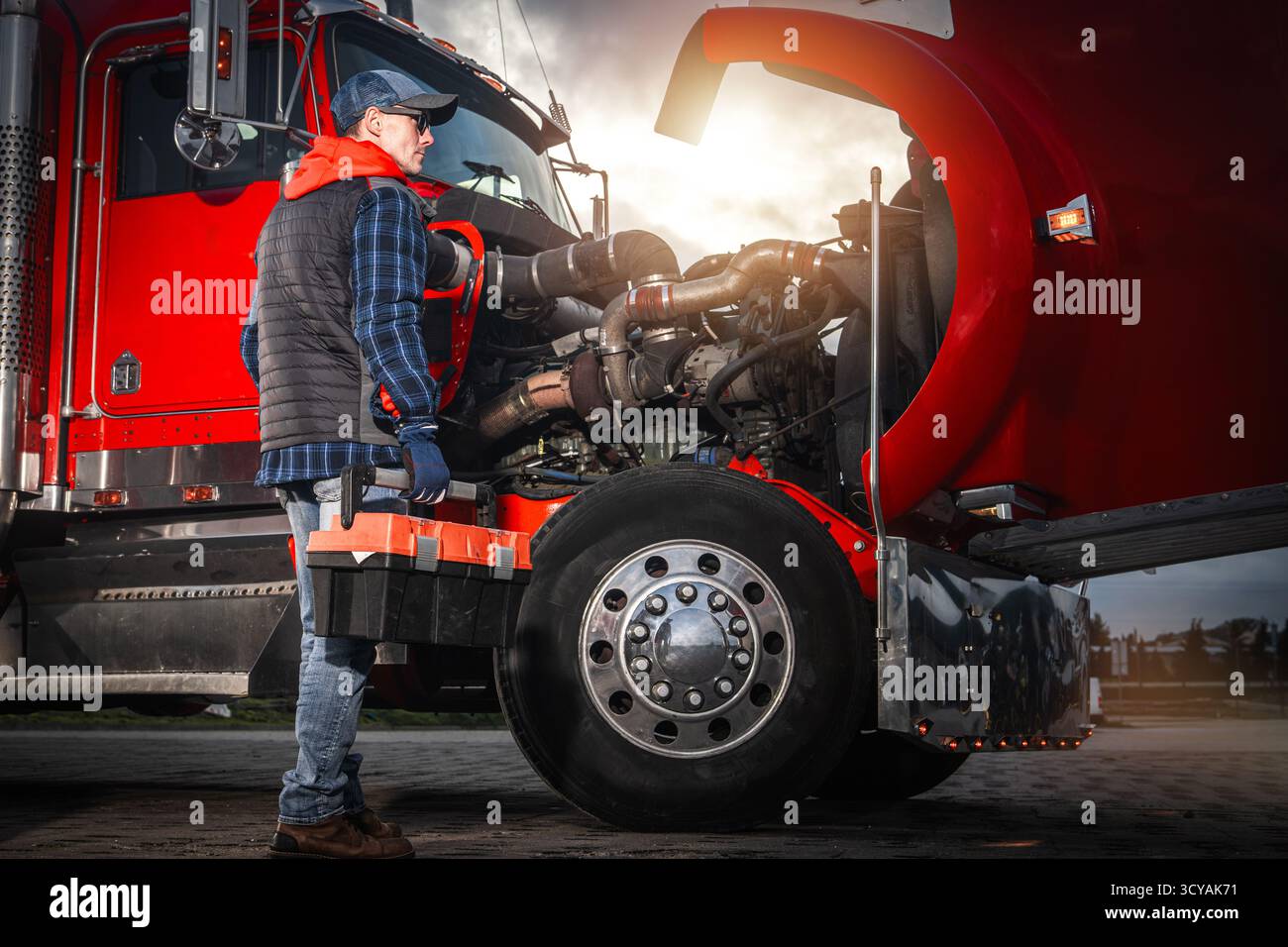 Un camionista ispeziona il motore di un grande carro di perforazione durante il tramonto, mostrando abilità e dedizione alla manutenzione del veicolo. Foto Stock