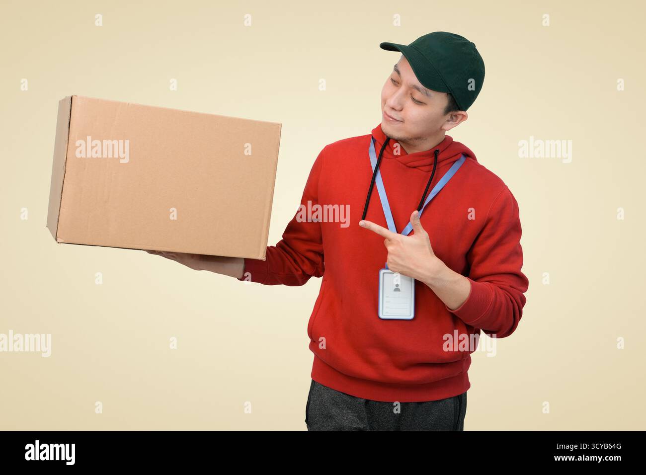 Un corriere sorridente in una felpa con cappuccio e cappuccio rosso può contenere e puntare la confezione sullo sfondo dello studio Foto Stock