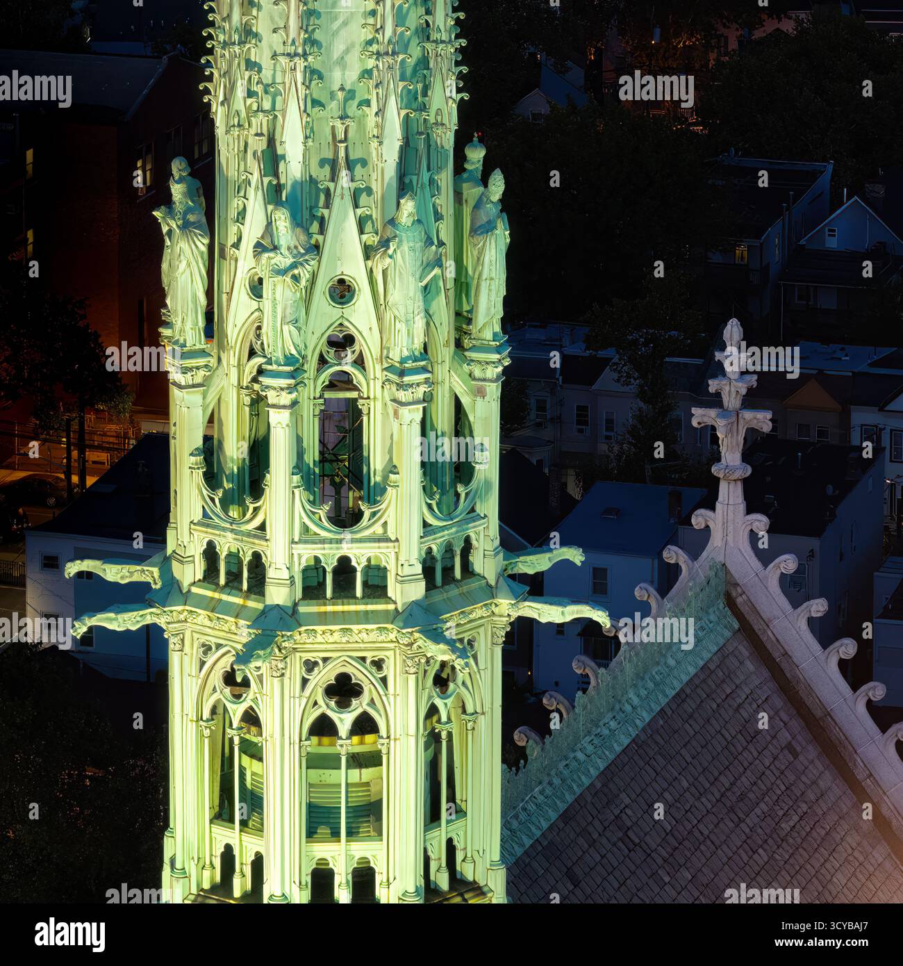 La guglia della cattedrale gotica della basilica del Sacro cuore è illuminata in modo intricato e mette in evidenza dettagliate sculture di santi. Il paesaggio urbano nel retro Foto Stock