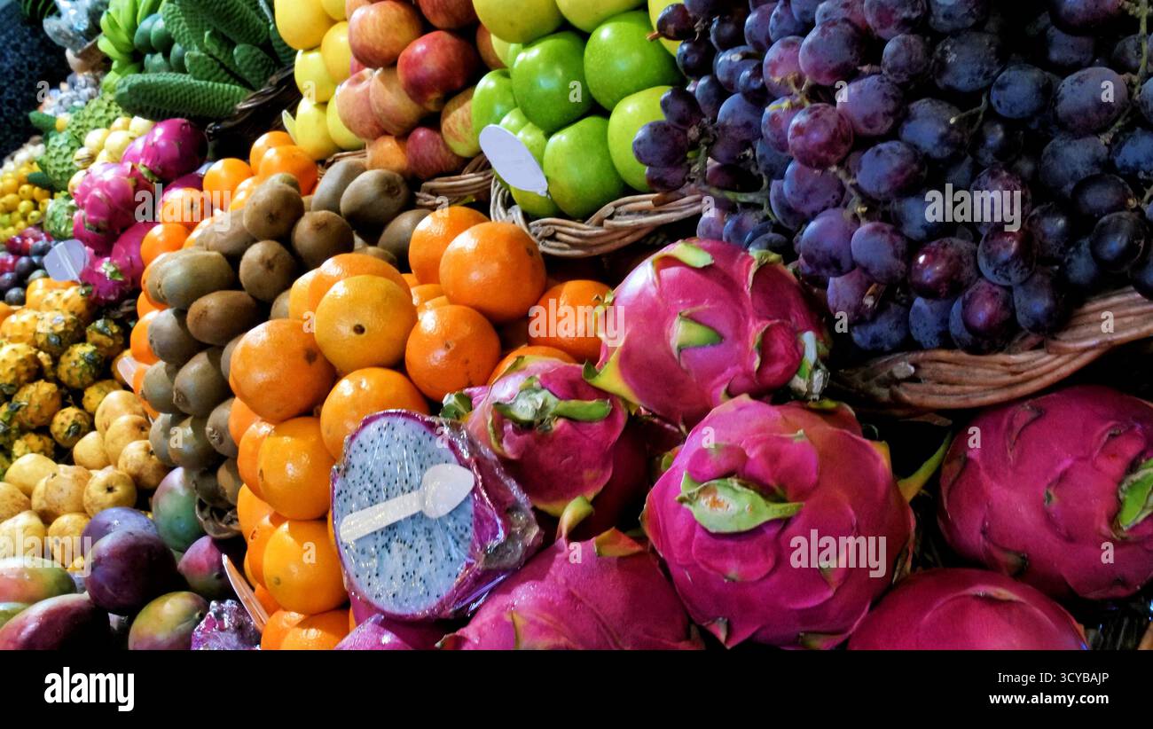 Colorato mercato di frutta tropicale con cesti di manghi, banane, cherimoya, avocado e agrumi. Esposizione di prodotti freschi con etichette dei prezzi. Ideale per chi ama Foto Stock