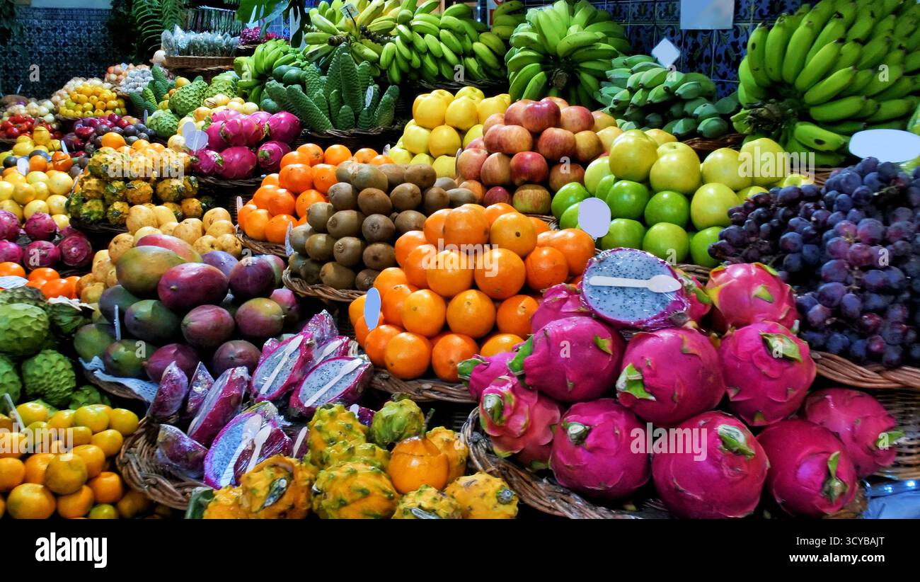 Colorato mercato di frutta tropicale con cesti di manghi, banane, cherimoya, avocado e agrumi. Esposizione di prodotti freschi con etichette dei prezzi. Ideale per chi ama Foto Stock